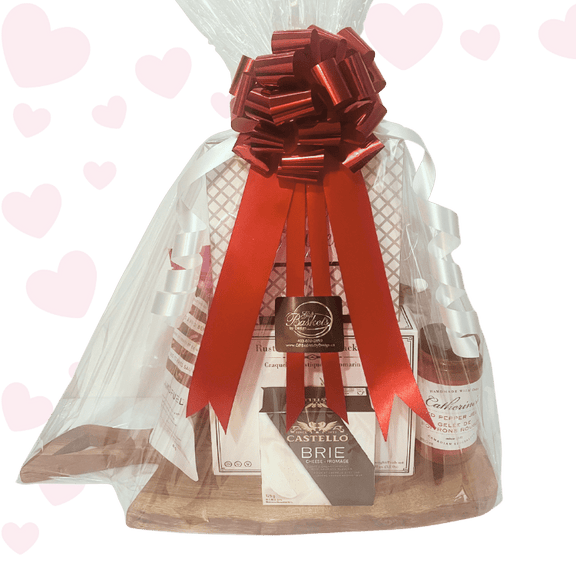 Love at First Bite Valentine’s charcuterie gift basket with gourmet crackers, brie cheese, chocolates, salmon, and sweet treats, beautifully packaged in cellophane with red ribbons and bow for Valentine’s Day