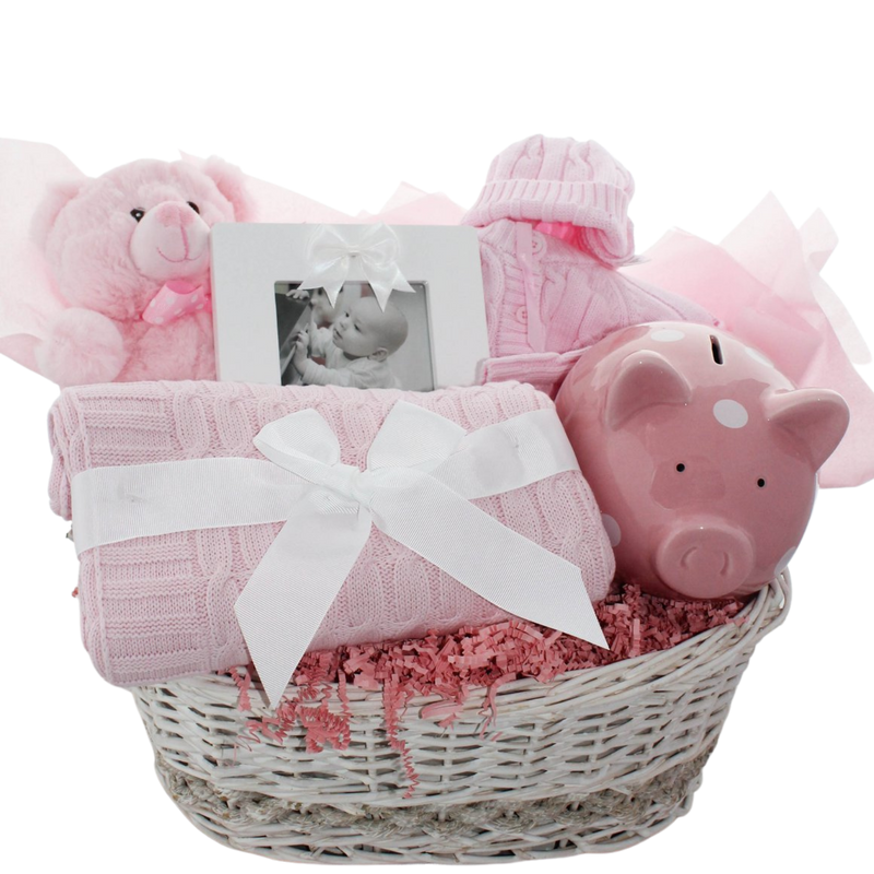 Hello Little One baby gift basket with sweater set, piggy bank, teddy bear, photo frame, and cable knit blanket in a wicker basket, shown in pink