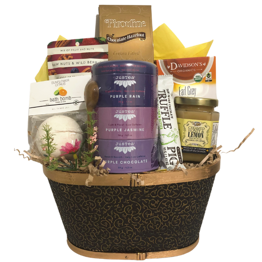 A calming gift basket featuring assorted teas, honey, a bath bomb, chocolate, and snacks, arranged in a black splitwood tray.